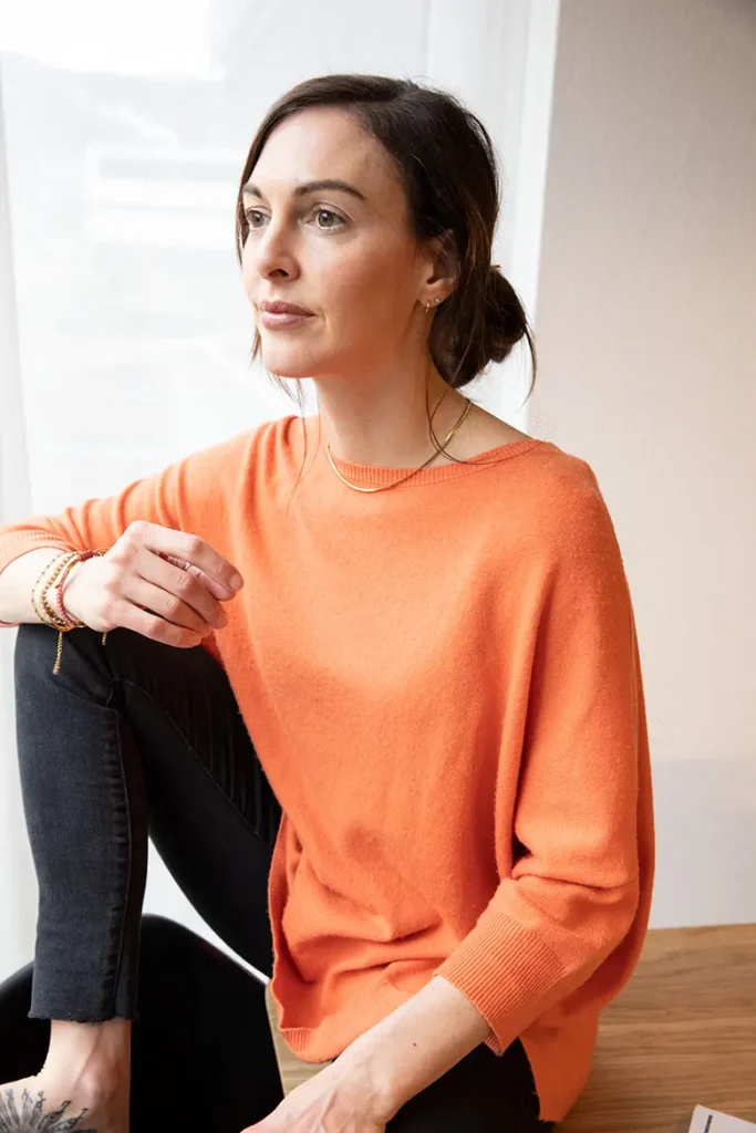 frau-oranger-pullover-sitzen-tattoo-fuss