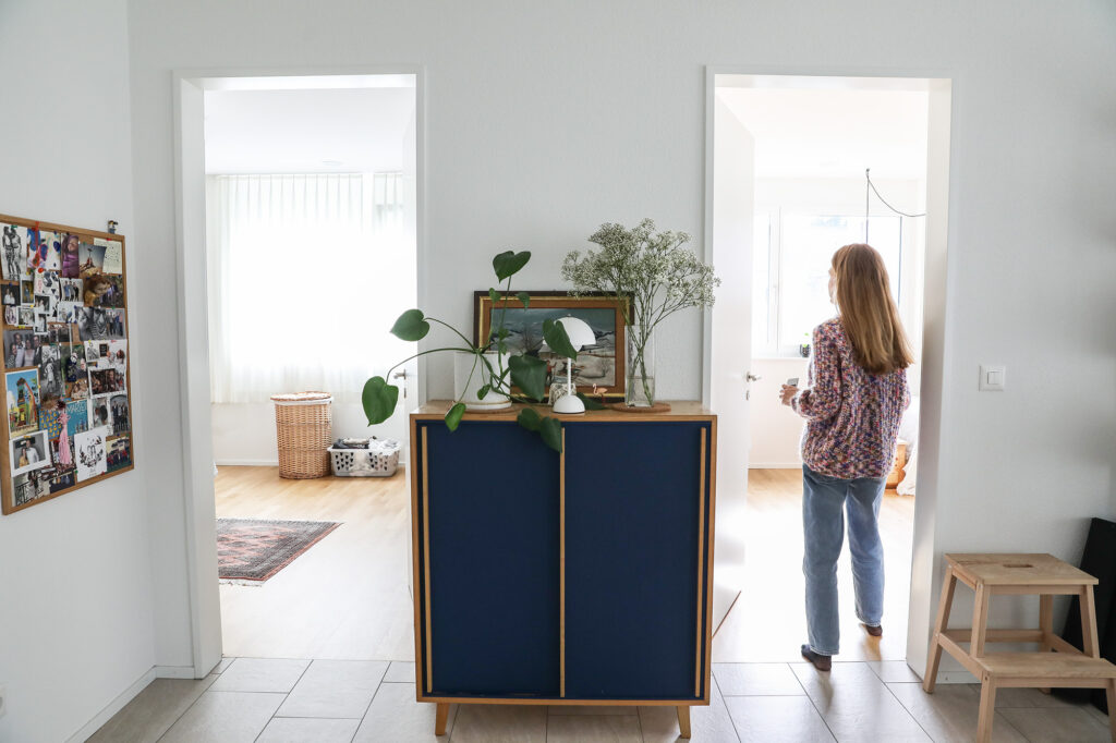 flur-tür-frau-wolljacke-jeans-kommode-pflanze-fotowand