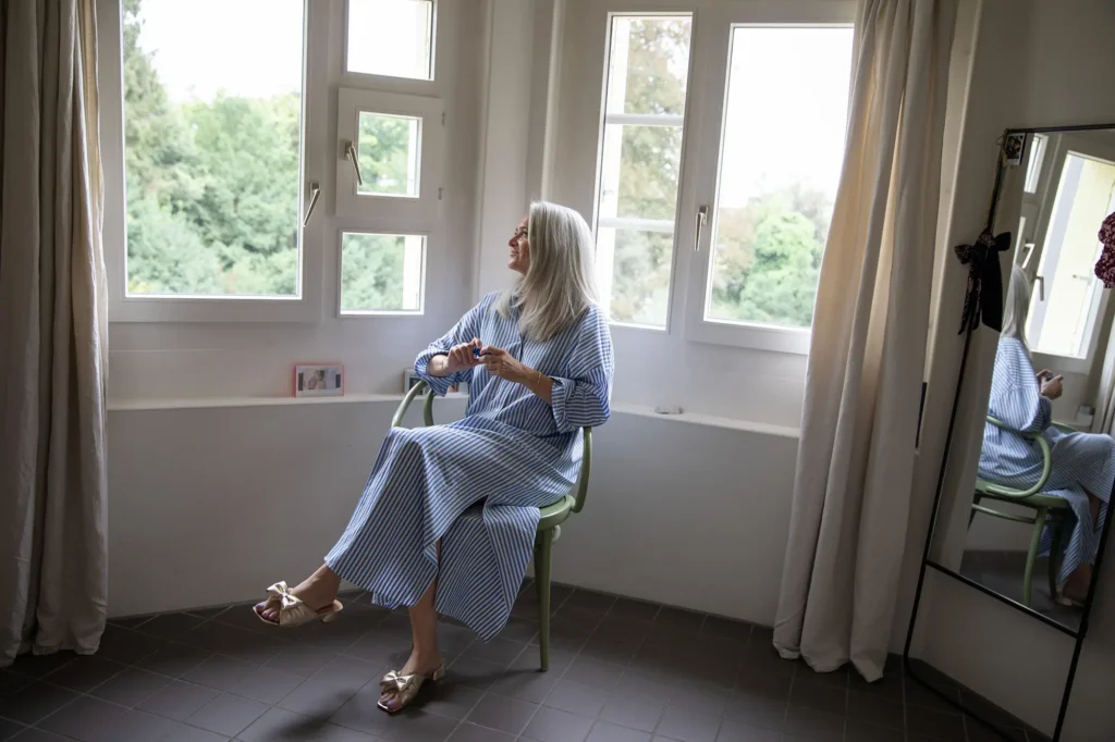 frau-gestreiftes-kleid-stuhl-fenster-aussicht-bäume