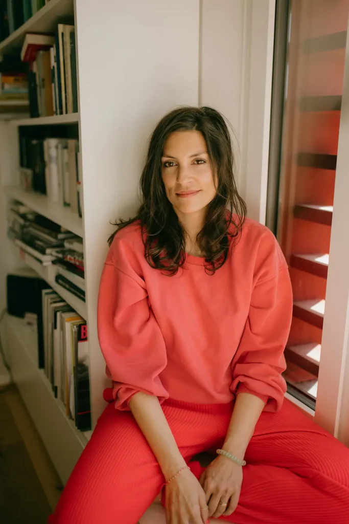 frau-dunkle-haare-oranger-pullover-fenstersims-porträt