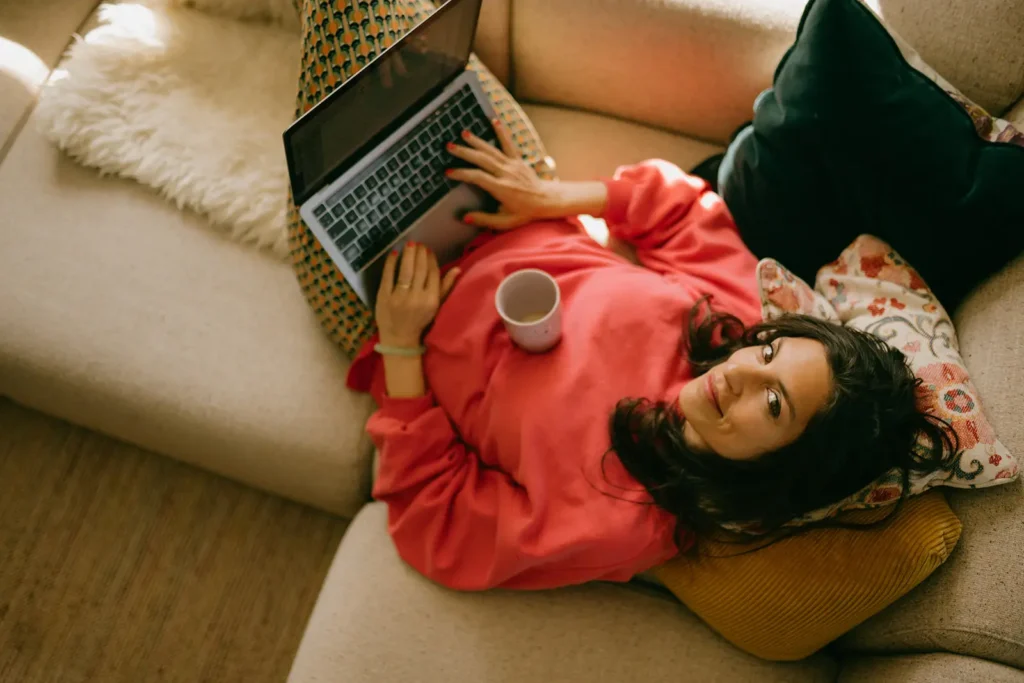frau-sofa-liegen-laptop-tee-tasse-kaffee-kissen