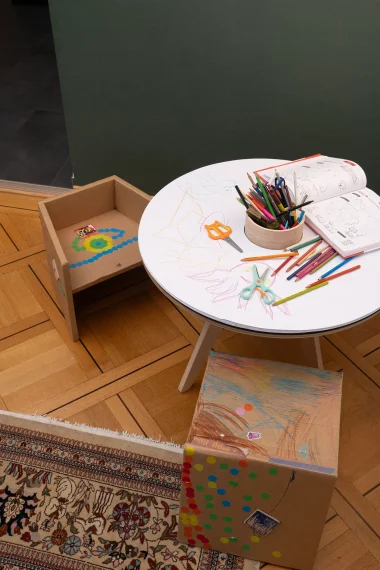 tisch-farbstifte-kinderstuhl-teppich-gruene-wand-parkett-schere